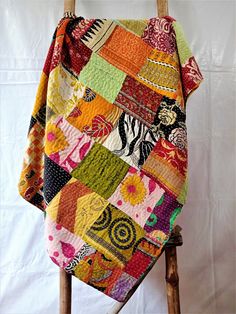 a multicolored patchwork blanket sitting on top of a wooden chair next to a white wall