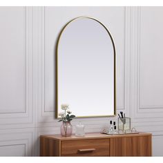 a mirror sitting on top of a wooden dresser next to a vase with flowers in it