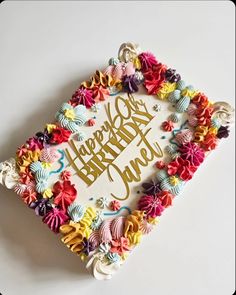 a happy birthday cake decorated with colorful flowers and ribbons on a white surface, in the shape of a square