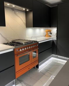 an orange stove top oven sitting inside of a kitchen next to black cabinets and counter tops