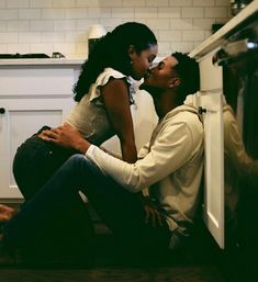 a man and woman kissing in front of an oven while sitting on the floor next to each other