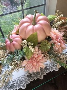 a vase filled with pink flowers and pumpkins on top of a glass table next to a window