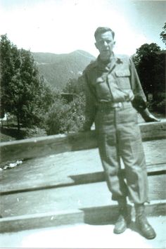 an old black and white photo of a man in uniform standing on a wooden deck