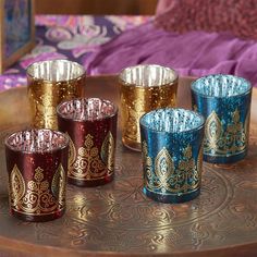 three different colored glass cups sitting on top of a metal tray next to a purple blanket