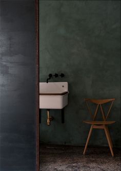 a white sink sitting next to a wooden chair in a green room with dark walls