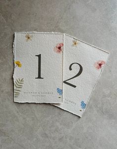 two cards with numbers and flowers on them sitting next to each other in front of a gray background