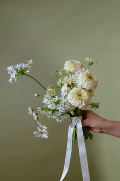 a person holding a bouquet of flowers with white ribbons around it's ends and the stems