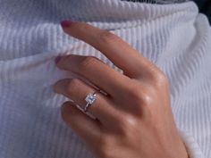 a woman's hand with a diamond ring on her left finger, wearing a white sweater