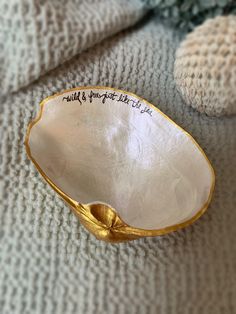 a white and gold bowl sitting on top of a bed next to a stuffed animal