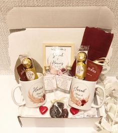 a white box with two coffee mugs and chocolates in it, along with other items