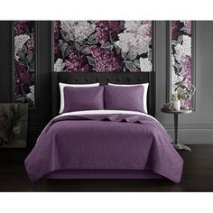 a bed with purple and white comforters in front of a floral wallpaper design