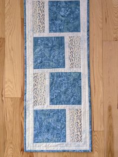 a blue and white quilted wall hanging on a wooden floor