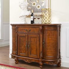 a wooden cabinet with two wine glasses on top and a vase filled with flowers next to it