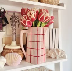 a pink vase with flowers in it sitting on a shelf next to books and shells