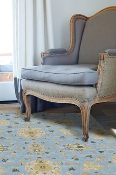 an old chair sitting on top of a rug in front of a window with curtains