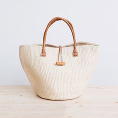 Rural Kamba women in Kenya hand-weave these beautiful handbags from tough sisal fibers. Sisal grows well in the semi-arid climate of eastern Kenya, and its spiky leaves contain long fibers that can be extracted for weaving.  approximate size: 10" diameter x 10" tall (without handle), 17" tall (with handle) leather hand Clothe Styles, Paris Wardrobe, Coastal Grandma, Rope Bag, Straw Handbags, Tuxedo Cat, Straw Bags, Leather Satchel Bag, Beautiful Handbags