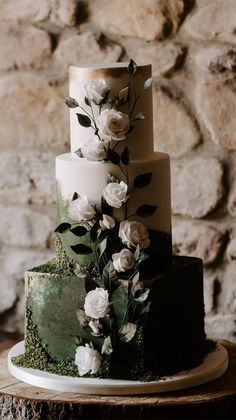 a three tiered cake with white flowers and greenery on the top is displayed against a stone wall