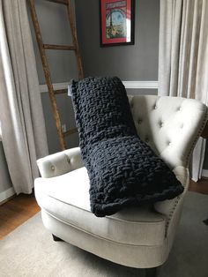 a white chair with a black blanket on it in front of a window and a ladder