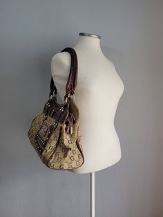 Make a statement with our Vintage Canvas and Leather Handbag in Brown and Gray by Gold Bags, a fusion of elegance and functionality. Crafted with meticulous attention to detail, this embellished zipped shoulder bag for women is adorned with crystals and rivets, adding a touch of glamour to your ensemble. The combination of brown leather and gray canvas lends a contemporary edge to its classic silhouette. Featuring a magnetic closure pocket on the front and a zipped pocket on the back, it offers Designer Tote Shoulder Bag With Metal Hardware, Designer Bags With Metal Hardware, Designer Hobo Tote Bag With Zipper, Elegant Hobo Tote Bag, Handheld Bags With Metal Hardware, Designer Shoulder Bag With Metal Hardware, Designer Tote Shoulder Bag With Zipper, Designer Tote Shoulder Bag With Zipper Closure, Elegant Pouch Shoulder Bag With Metal Hardware