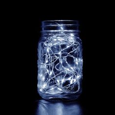 a mason jar filled with fairy lights on top of a black table next to a wall