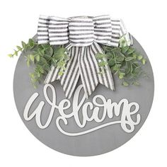 a welcome sign with a bow and greenery on it's side, in front of a white background