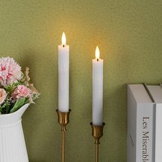 two white candles sitting on top of a table next to a vase filled with flowers