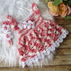 a crocheted baby dress and booties on a fur rug