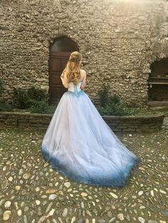 a woman wearing a blue and white dress standing in front of a stone building