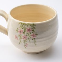 a white cup with pink flowers painted on the outside and inside, sitting on a white surface