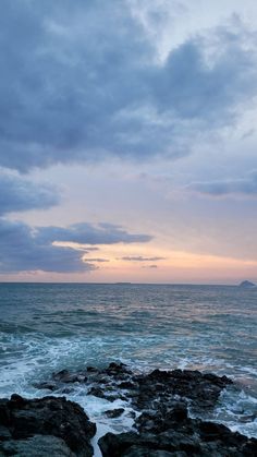 an ocean view with waves crashing on the rocks and clouds in the sky above it