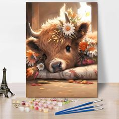 a painting of a cow with flowers on it's head is next to some paintbrushes