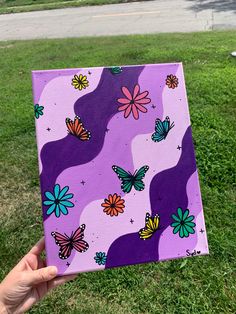 a hand holding up a purple square with colorful butterflies on it and grass in the background