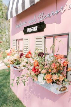 flowers are hanging from the side of a pink building that is painted pink and white