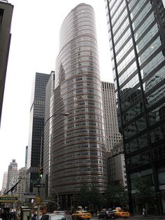 a city street filled with lots of tall buildings next to traffic and people walking on the sidewalk