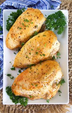 two pieces of chicken with parsley on a white plate next to a blue and white towel