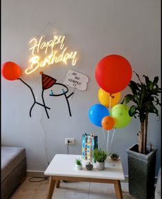 balloons are floating in the air near a table with a cake and potted plant