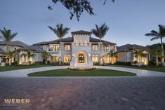 a large white house with palm trees in the front yard and driveway at night time