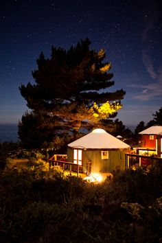 some tents are lit up at night by the water and trees in front of them