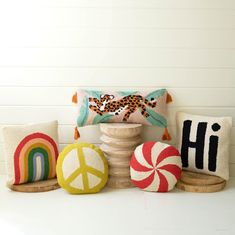 decorative pillows and pillow covers on a pedestal in front of a white wall, including a peace sign