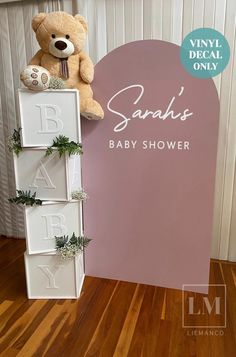 a teddy bear sitting on top of a baby shower sign next to a wooden floor