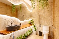 a bathroom with a sink, toilet and plants on the wall above it is illuminated by lights