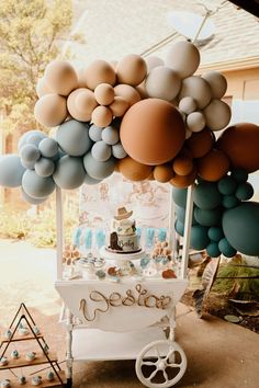 a cart with balloons and cake on it sitting in front of a house next to a tree