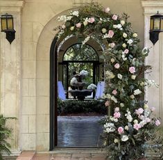 an archway with flowers and greenery on the outside, leading into a formal garden