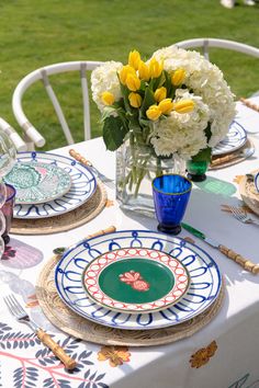 the table is set with plates and flowers in vases on it, along with other place settings