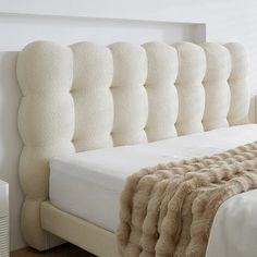 a bed with a white headboard and beige fur on the bottom part of it