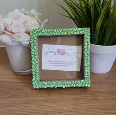 a small green frame sitting on top of a wooden table next to a potted plant