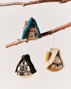 three ornaments hanging from a tree branch with houses on them and one has a blue roof