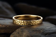 a gold wedding ring sitting on top of a rock next to a black stone wall