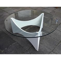 a glass table with a curved design on the top, sitting on a brick sidewalk