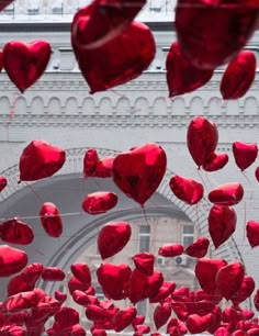 many red heart shaped balloons floating in the air near a building with arches and windows